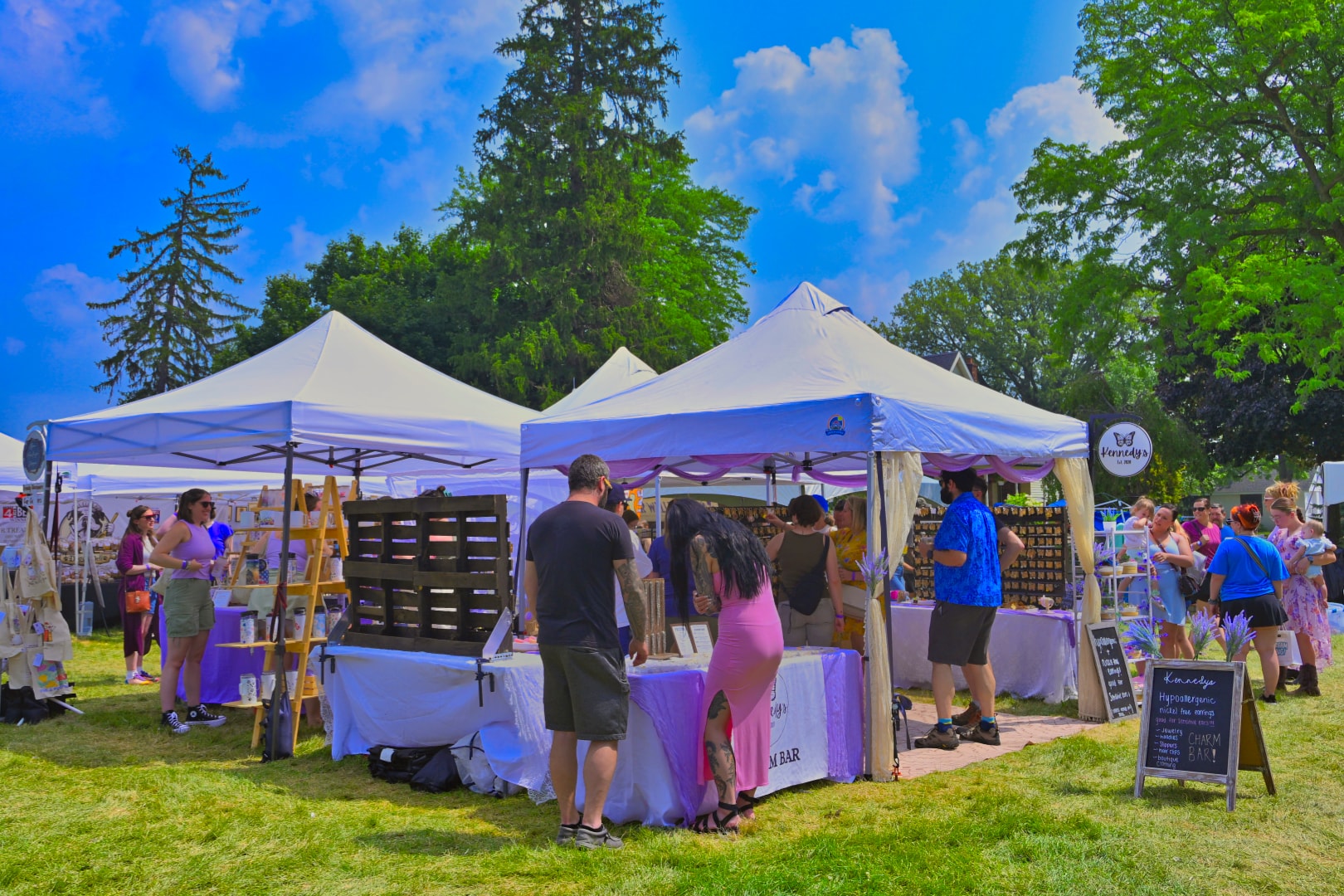 Festival attendees browsing Kennedy's hypoallergenic charm bar and lavender vendor stalls under white canopy tents at Blake's Lavender Festival, Blake's Apple Orchard, Armada Michigan — outdoor festival and event photography by Atelier Lens LLC