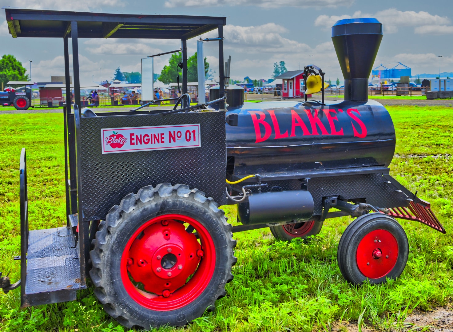Blake's Engine No. 01 custom steam engine display piece with red wheels and bold Blake's branding, set against the open grounds of Blake's Apple Orchard, Armada, Michigan — commercial property photography by Atelier Lens LLC