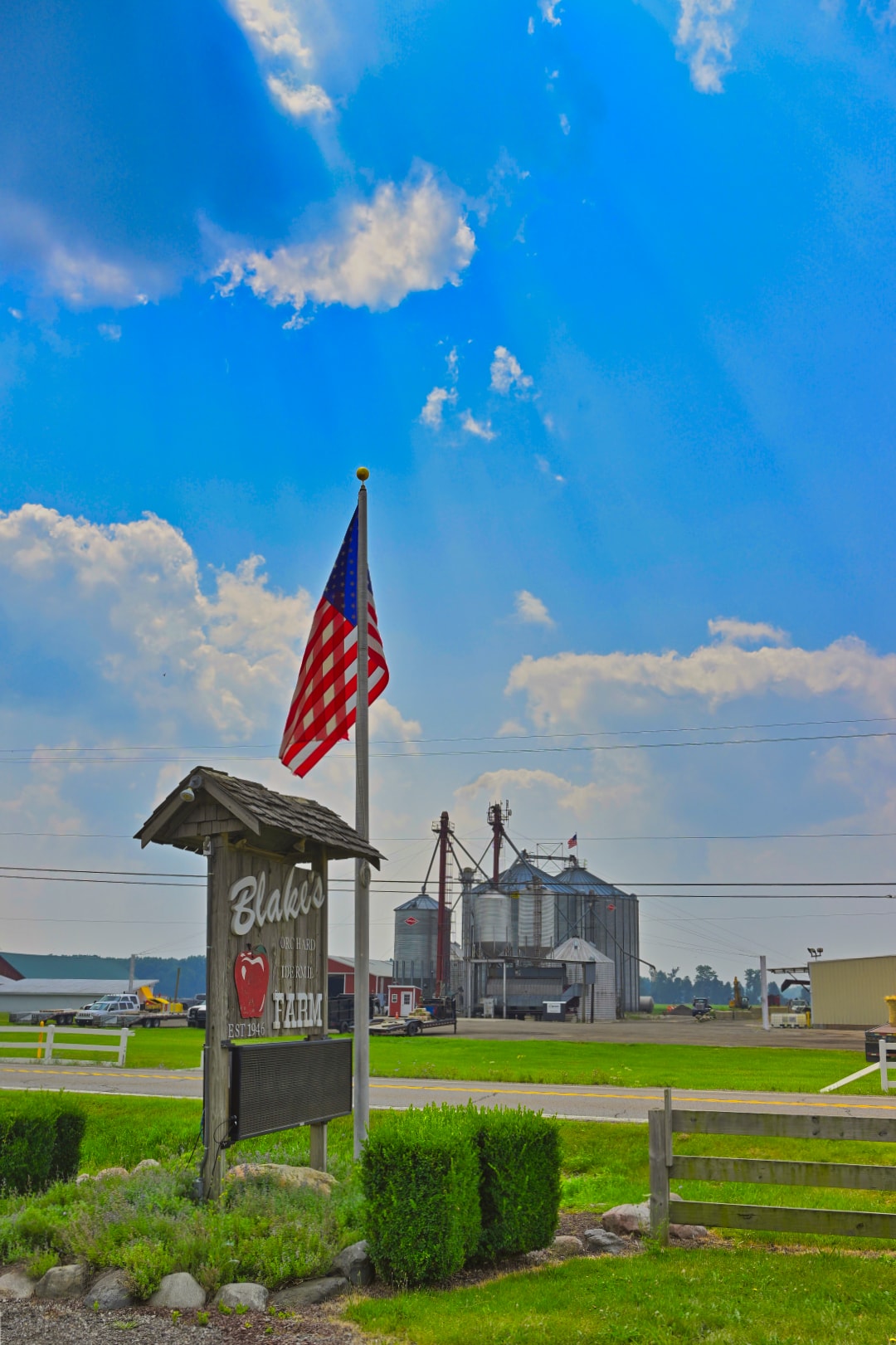 Blake's Orchard Farm roadside sign established 1945 with American flag and grain storage silos in the background — commercial property and agricultural architecture photography, Armada, Michigan by Atelier Lens LLC